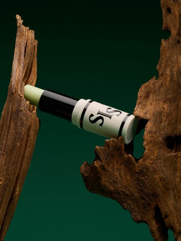 Un stick de parfum ouvert. La formule est de couleur verte claire tintée par de la spiruline. Le stick tient entre 2 branche des de bois et le fond est vert, pour rappeler le côté vert et florale de ce parfum