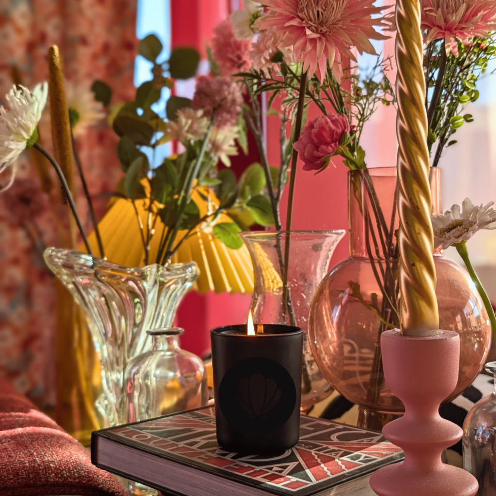 La bougie Ici c'est le sud, est posée sur des livre avec un fond rose